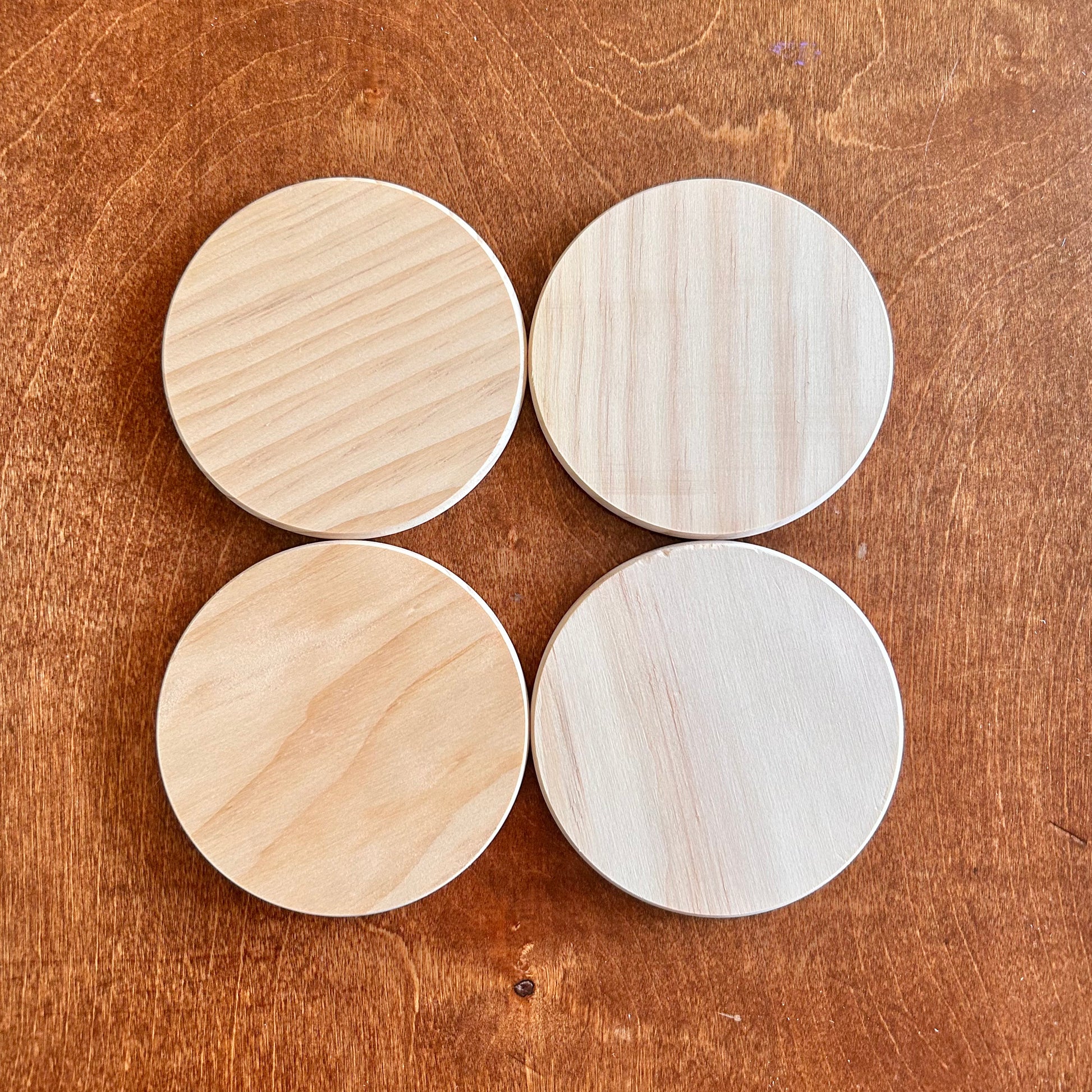 Four round wooden coasters on a wooden surface