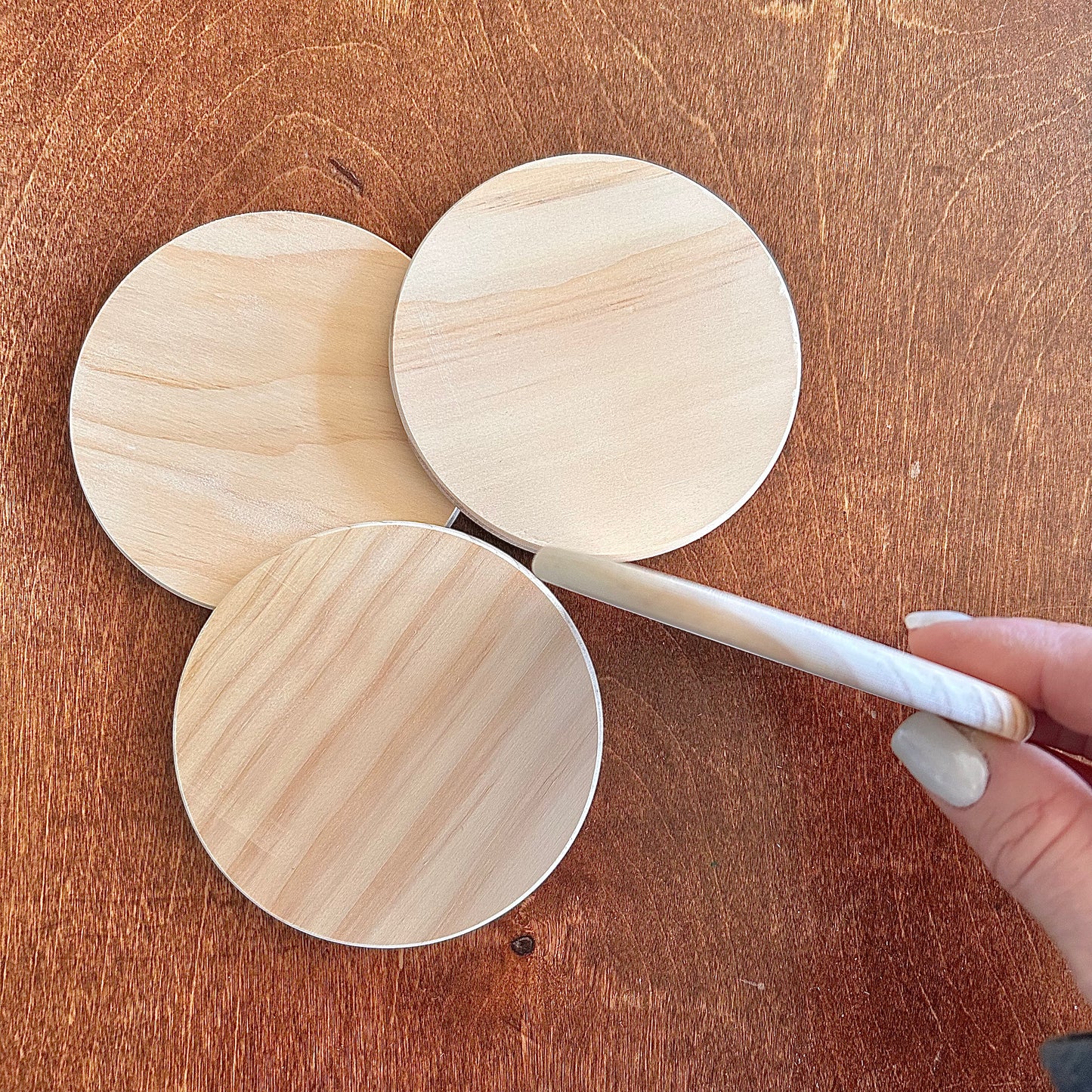 Three wooden coasters on a wooden surface with a hand holding one coaster on it's side