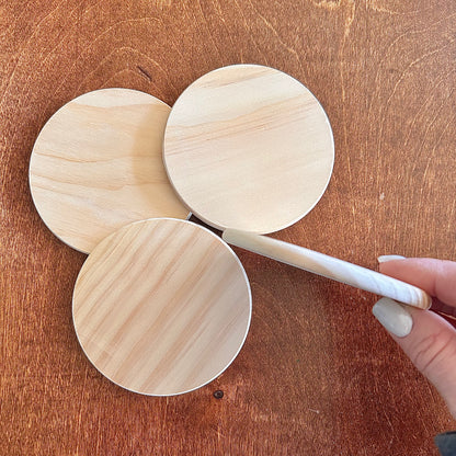 Three wooden coasters on a wooden surface with a hand holding one coaster on it's side