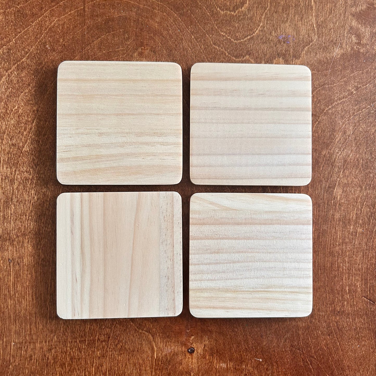 Four square wooden coasters on a wooden surface
