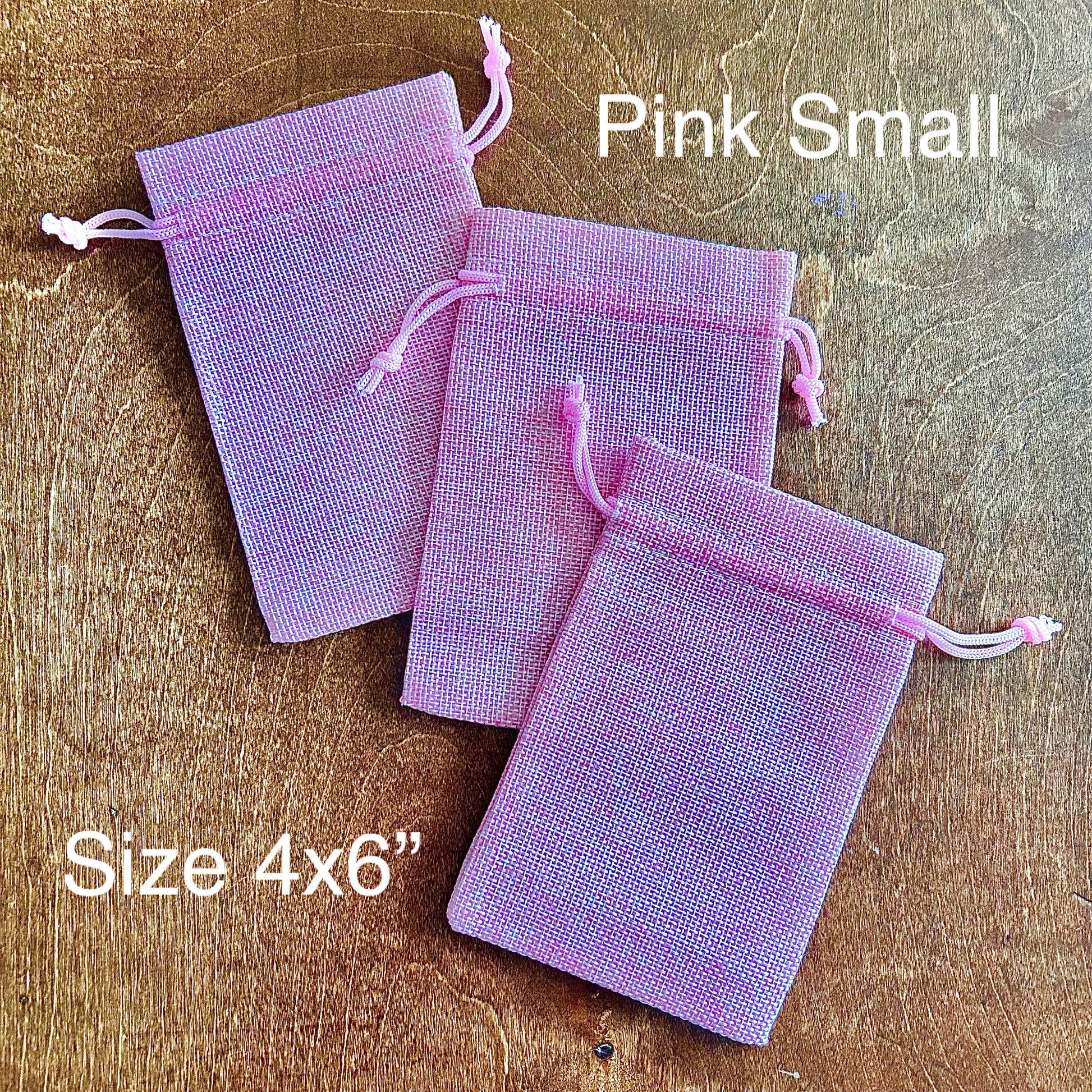 Three small pink drawstring bags on a wooden surface with text indicating size and color.
