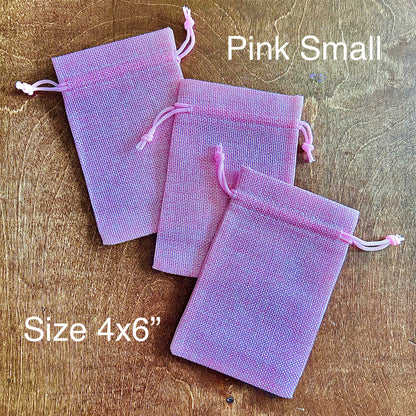 Three small pink drawstring bags on a wooden surface with text indicating size and color.
